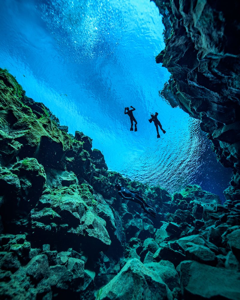 Two people swimming in Slifra Fissure in Iceland.